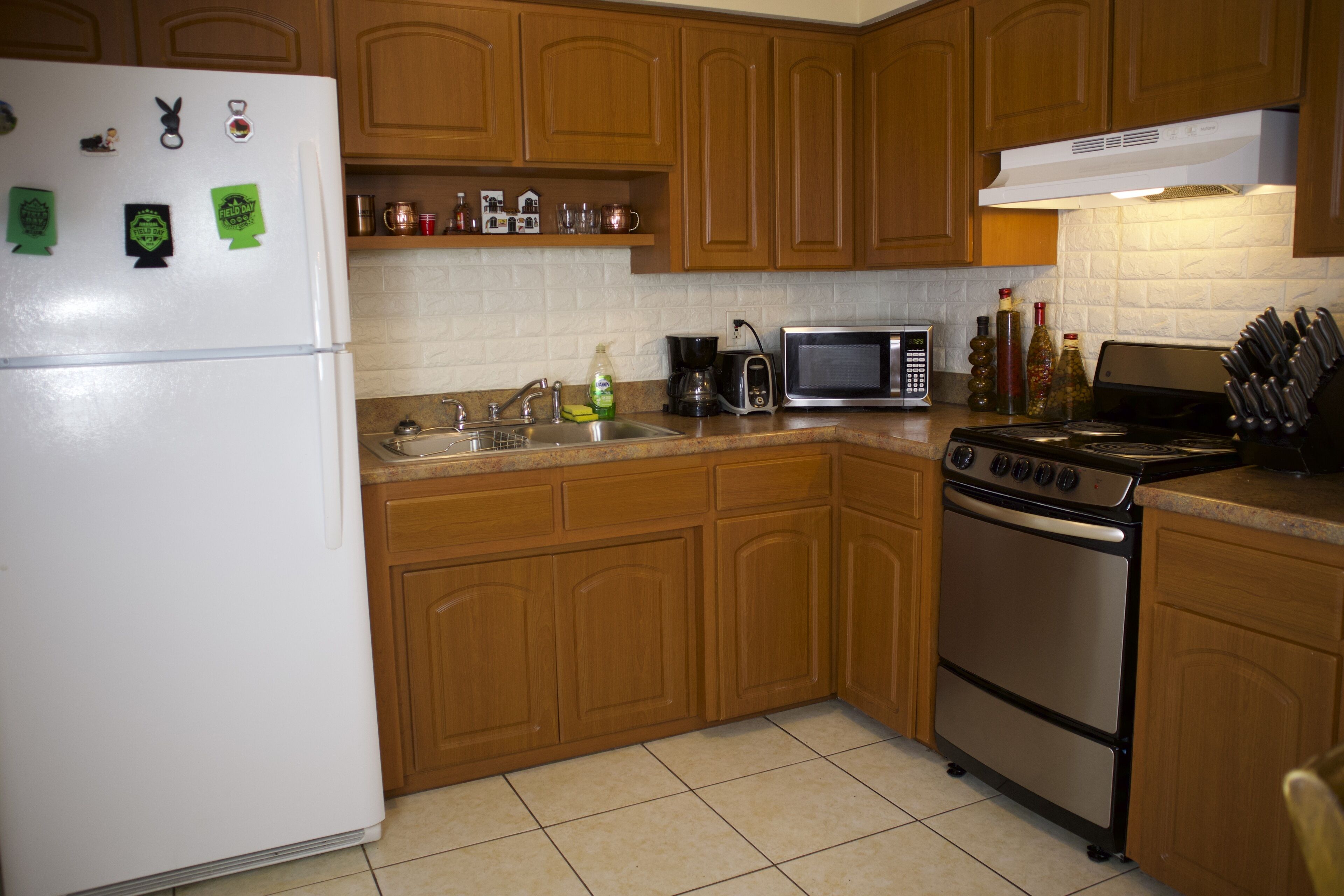 Una cocina con armarios de madera, un refrigerador blanco, un microondas, una estufa y un lavabo.