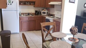 Una cocina con armarios de madera, refrigerador, estufa, microondas y una mesa de comedor con sillas.