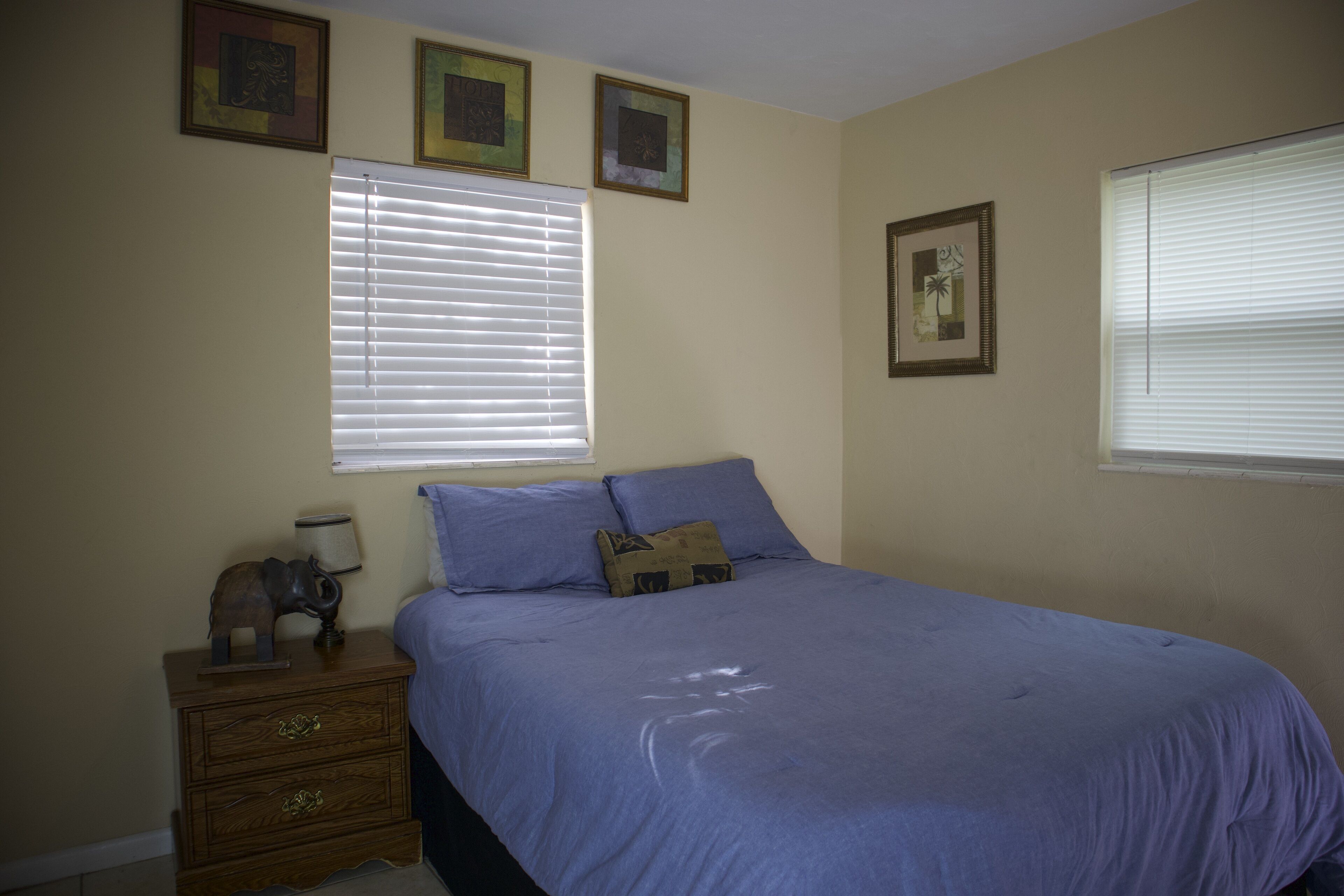 A bedroom with a bed, a nightstand, and a window with blinds.