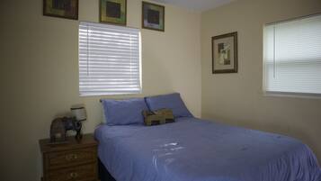 A bedroom with a bed, a nightstand, and a window with blinds.