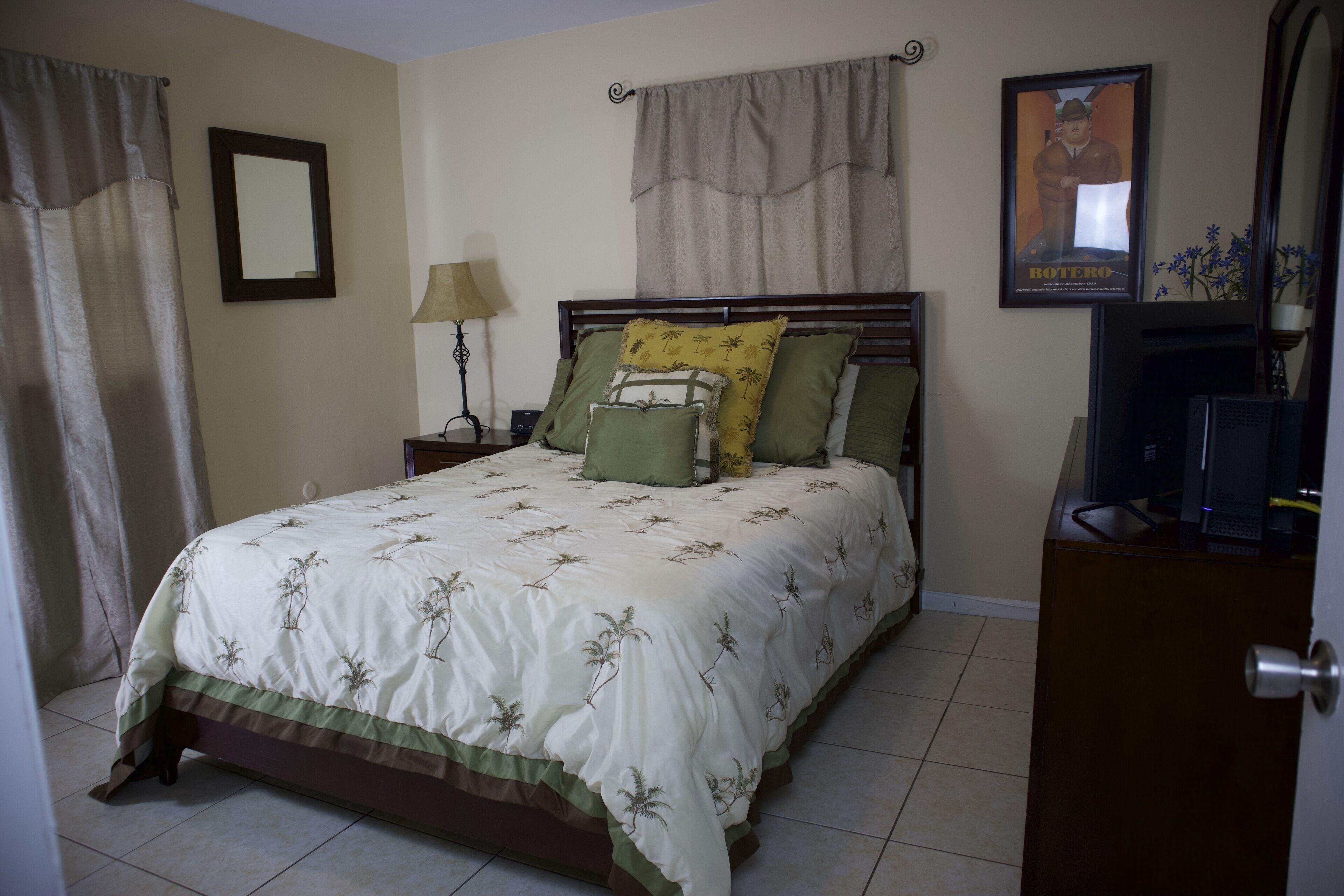 A neatly made bed with a floral bedspread, a bedside lamp, and a framed picture on the wall.
