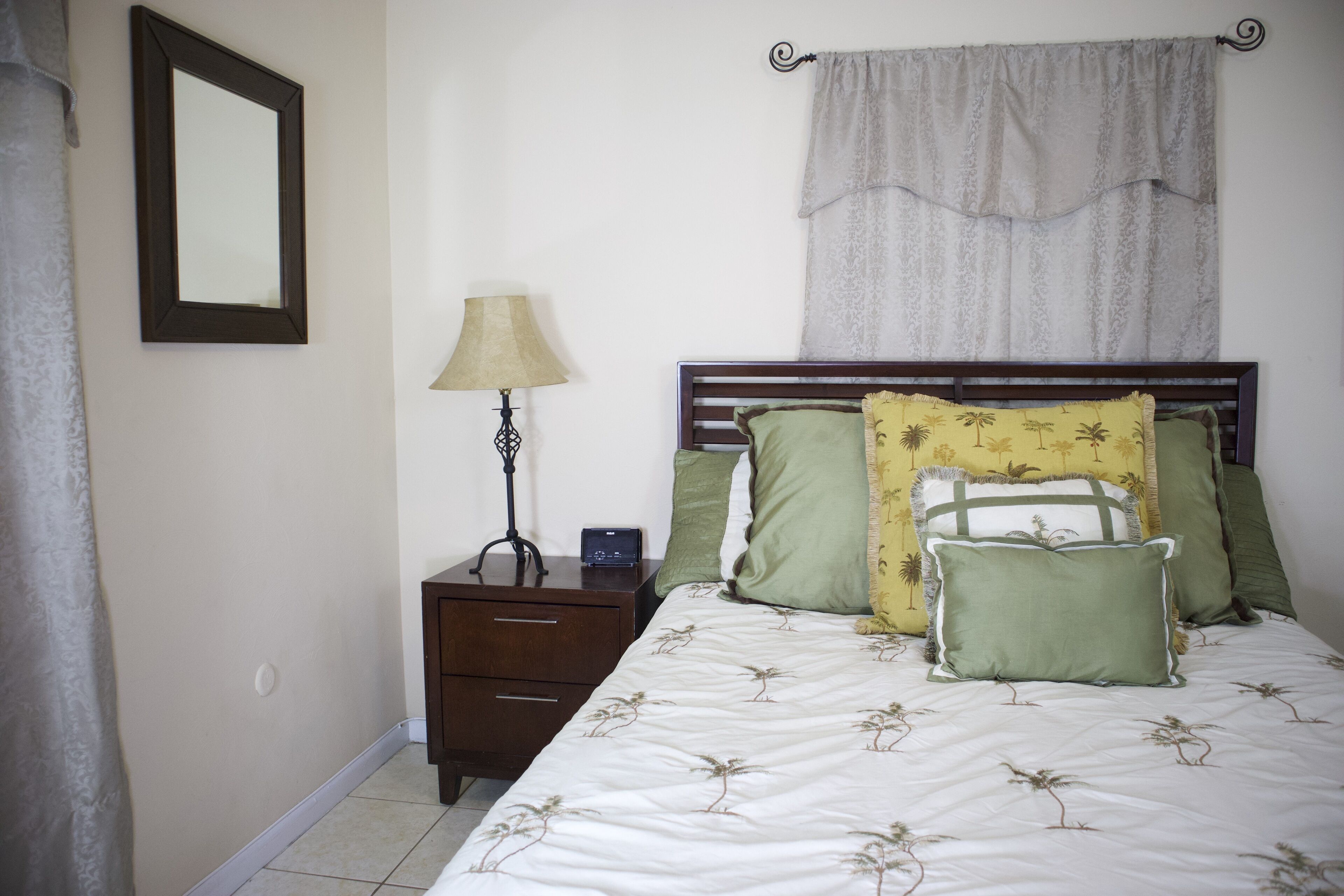 A bedroom with a bed, a nightstand, a lamp, a mirror, and a window with curtains.