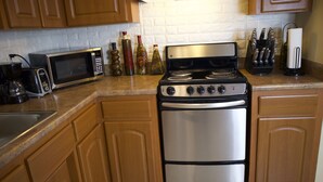 Una cocina con armarios de madera, estufa de acero inoxidable, microondas y varios utensilios de cocina sobre la encimera.