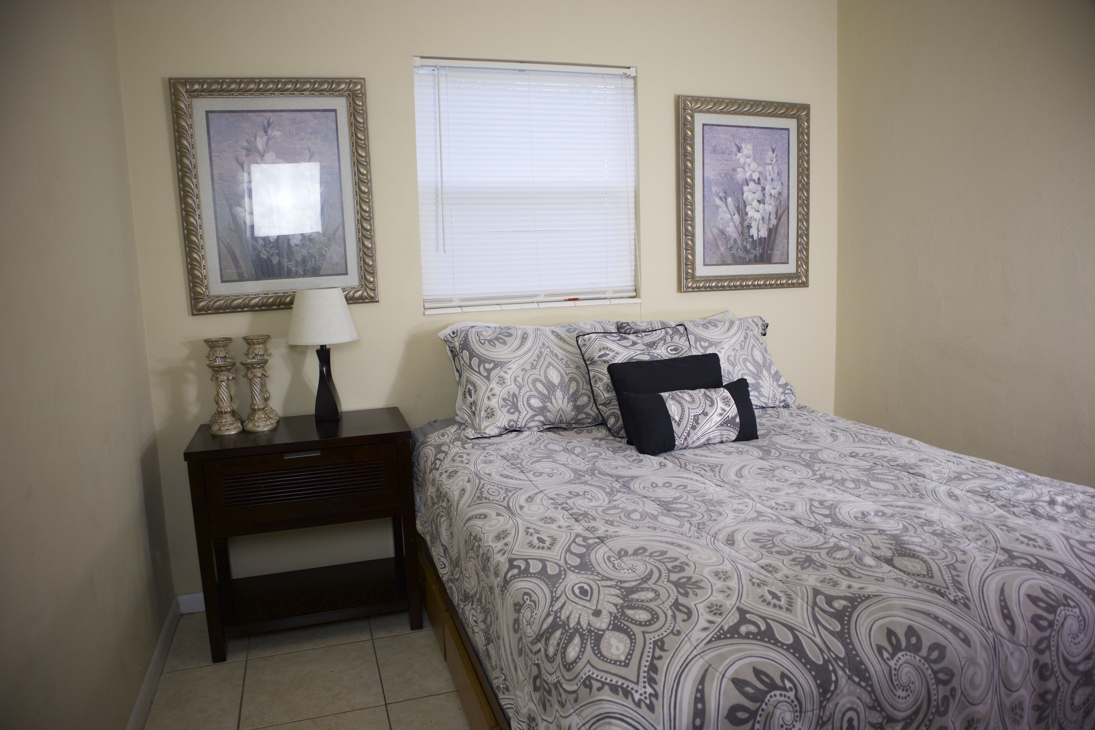 Quarto com cama, mesa de cabeceira, luminária e duas fotos emolduradas na parede.
