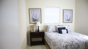 Un dormitorio con una cama, mesita de noche, lámpara y dos cuadros en la pared.