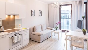 A modern, well-lit apartment with a kitchenette, a sofa, a dining table, and a balcony with curtains.