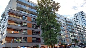 A multi-story building with balconies, large windows, and a tree in front.