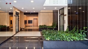 A modern lobby with a glass wall, a reception desk, and a plant area.