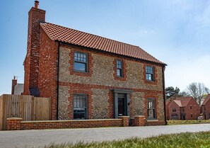 Stunning two-story home with a brick and stone facade, featuring a central entrance and a charming wooden fence.