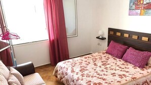 Ein Schlafzimmer mit Bett, Stuhl, einem Fenster mit Vorhängen und einer Wandlampe.