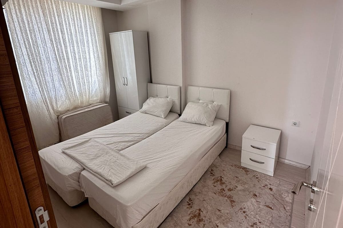 A bedroom with two beds, a wardrobe, a bedside table, and a small cabinet.