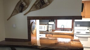 A kitchen with a wooden bar counter, stools, a microwave, a coffee maker, and a stove.