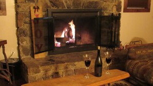 A cozy living room with a stone fireplace, a wooden table with glasses and a bottle, and a patterned rug.