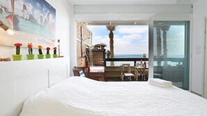 Un dormitorio con una cama grande, un balcón con mesa y sillas, y vista al mar.