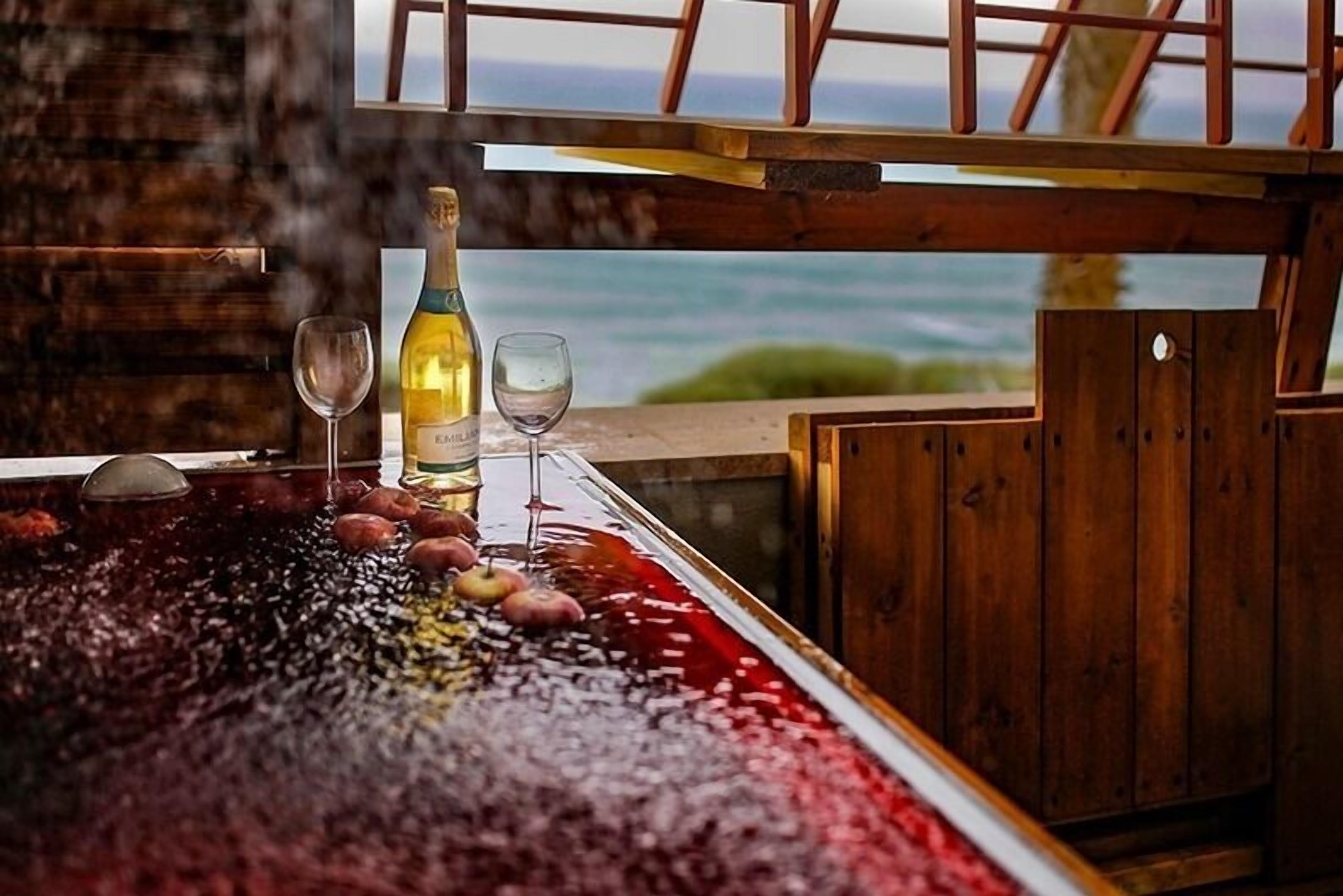 Un comptoir en bois donnant sur l’océan, une bouteille de vin et deux verres posés sur une table.