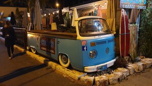 Ein alter, blauer Van ist an der Straße geparkt, mit der Aufschrift "Cody's Coffee Shack" sowie Social-Media-Symbolen und dem VW-Logo.