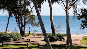 Ein Park direkt am Strand mit Bänken, einem Schild und Palmen.
