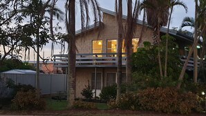 Ein zweistöckiges Haus mit Balkon, umgeben von Palmen und einem eingezäunten Garten.