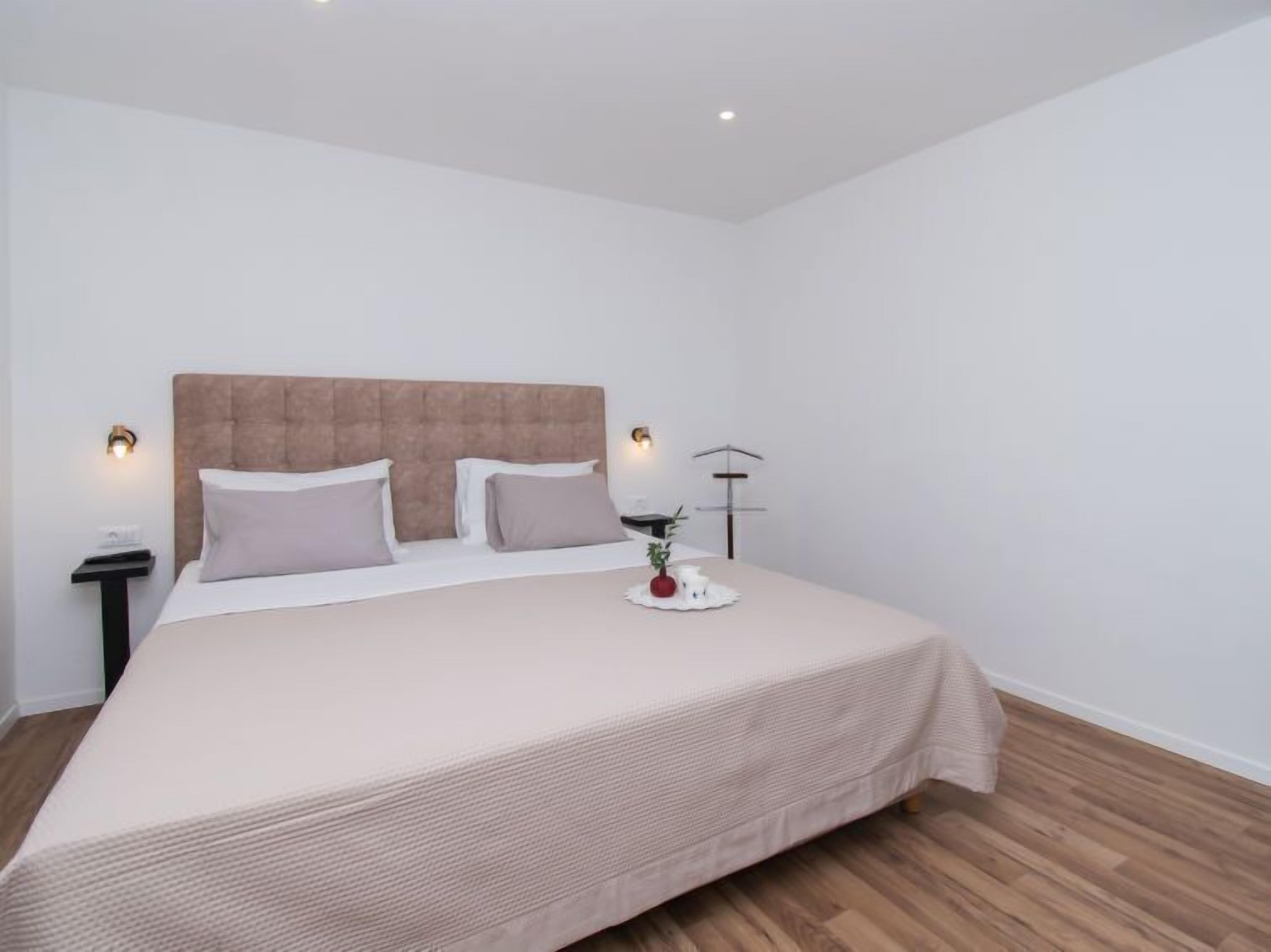 A neatly made bed with a headboard, two bedside tables with lamps, and a bedside plant.