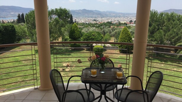 A balcony with a table and chairs, overlooking a cityscape and greenery.