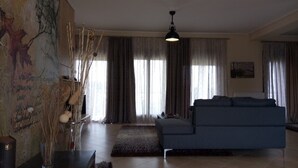 A living room with a blue sofa, a hanging light fixture, and a large window with curtains.
