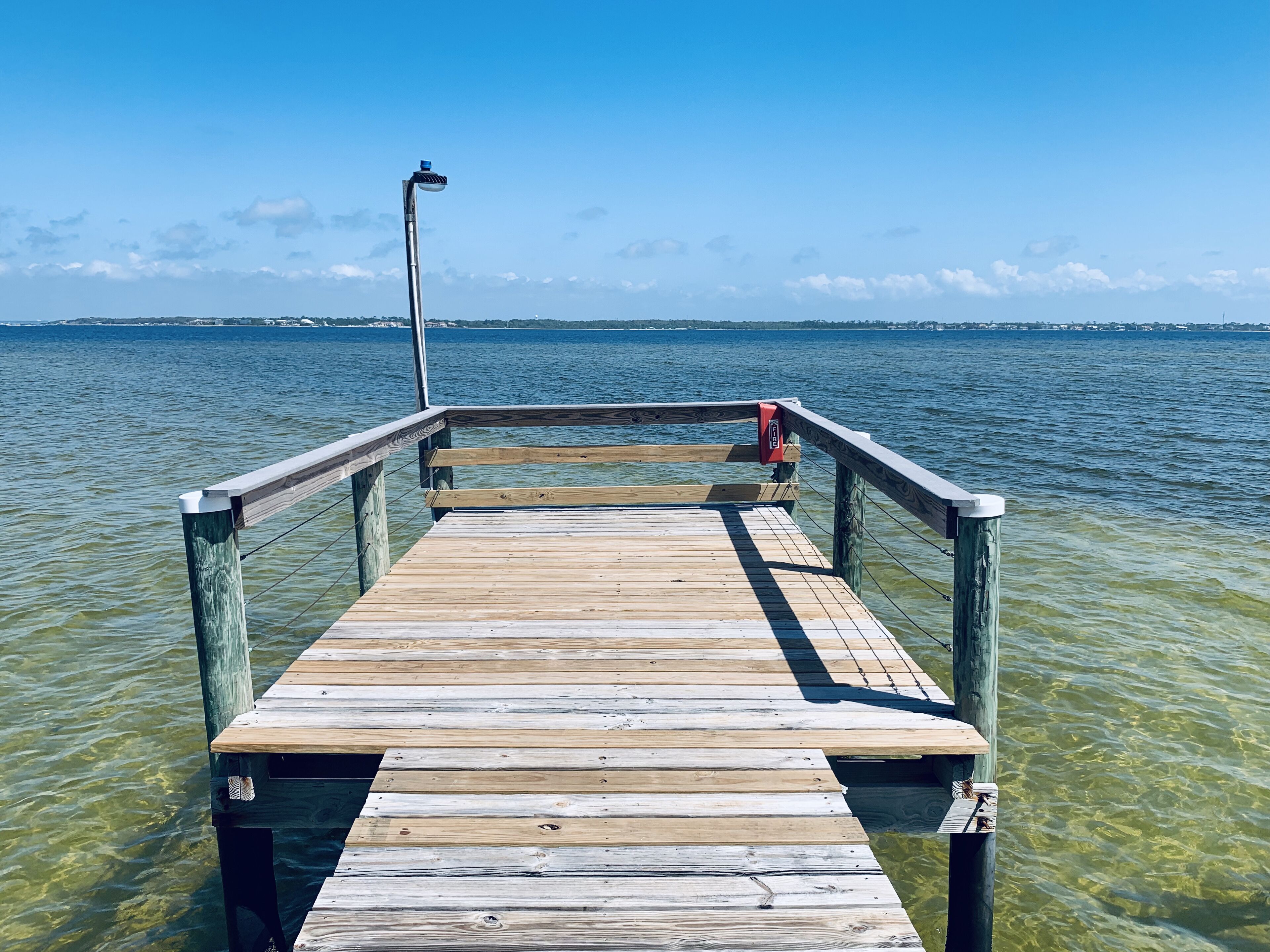 Eine Holzstege, der sich über ein Gewässer erstreckt, mit blauem Himmel darüber.