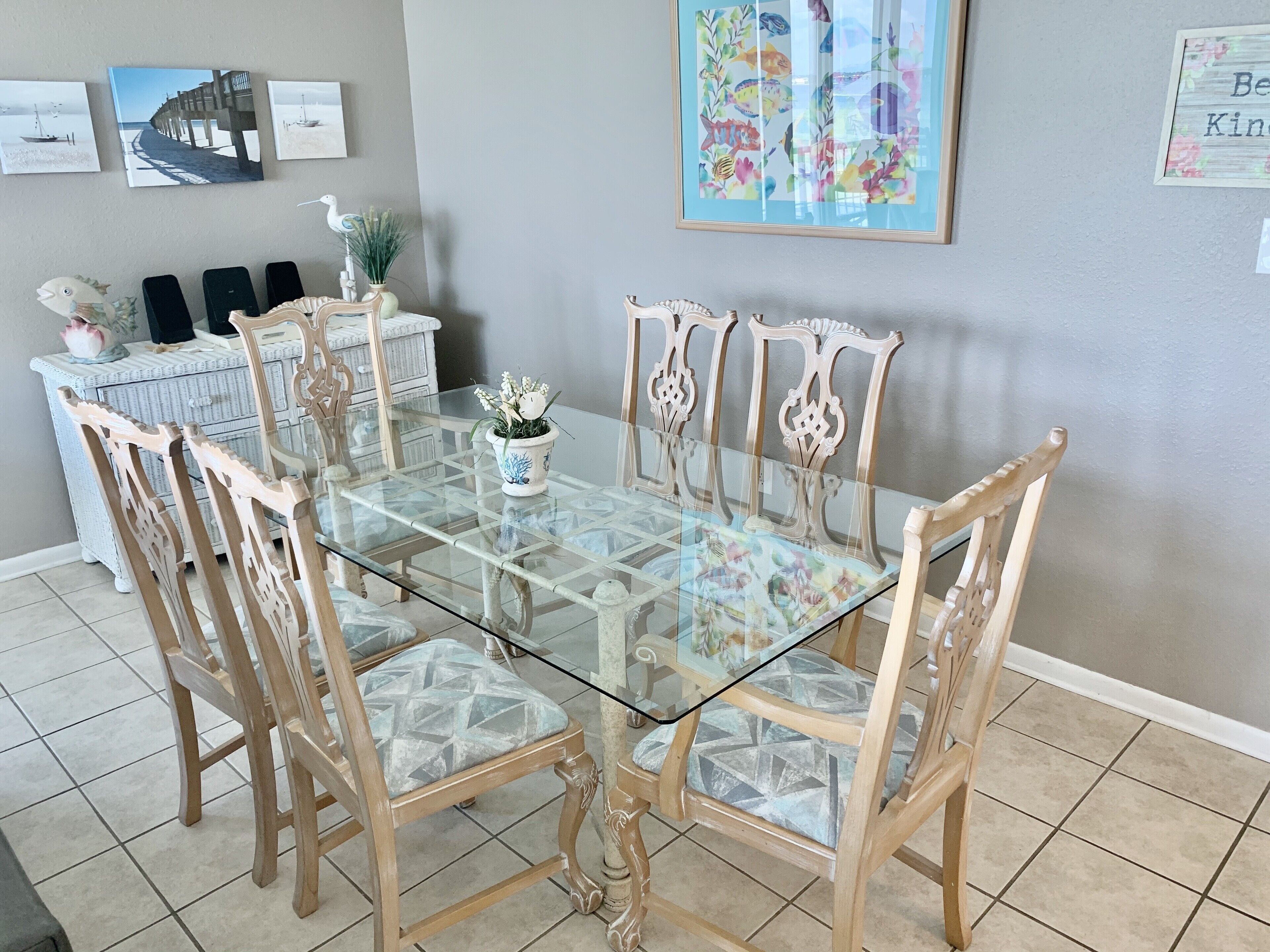 Comedor con mesa de vidrio rodeada de sillas de madera con asientos acolchados.