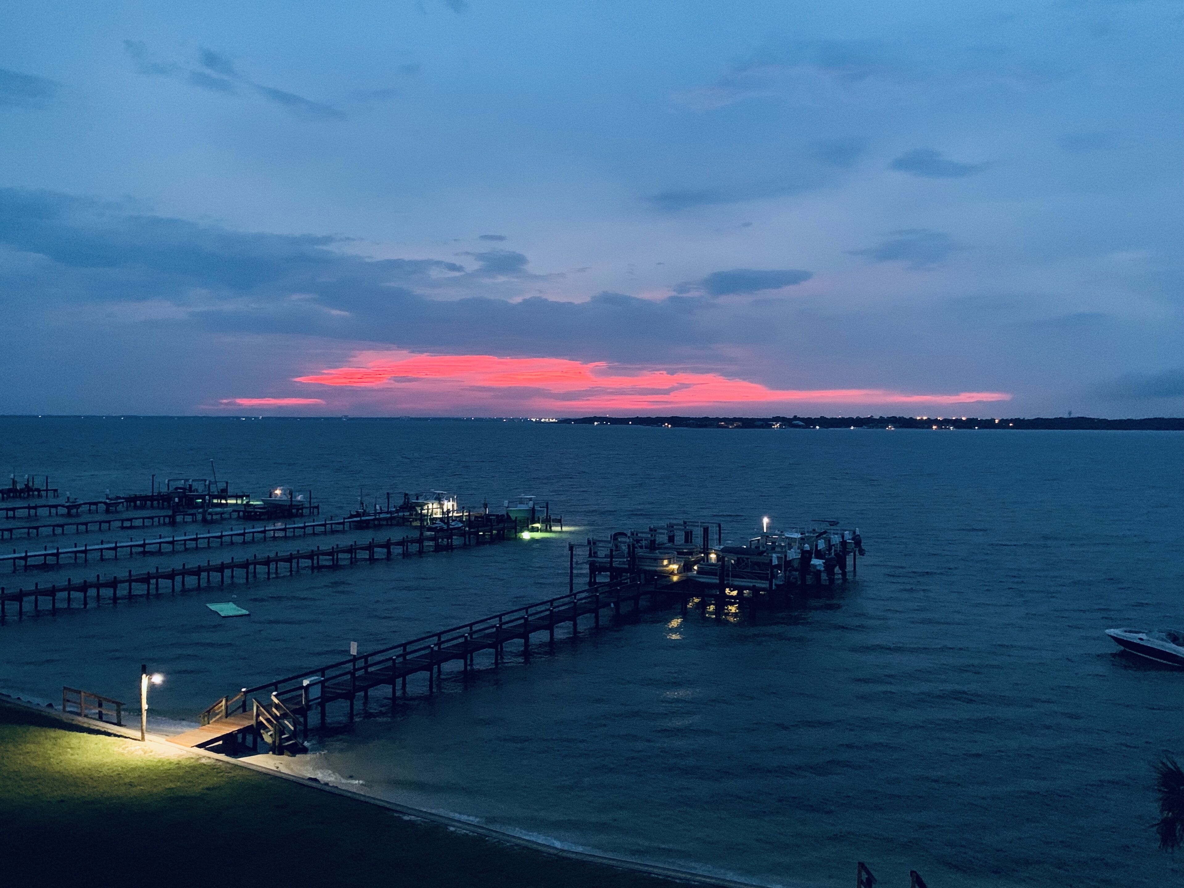 Un muelle se adentra en aguas tranquilas al anochecer bajo un cielo rosado.