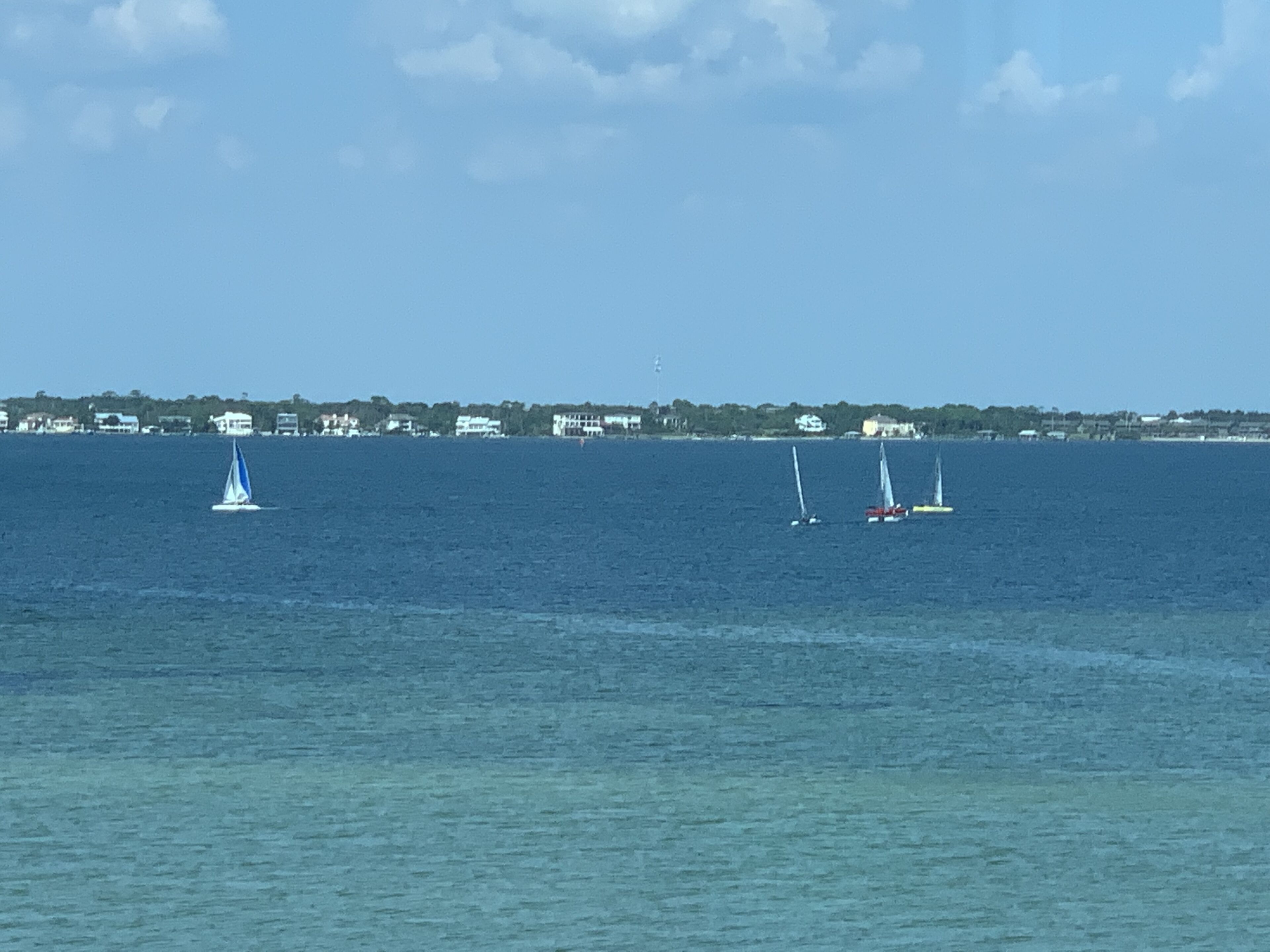 A coastal view with sailboats on the water and a row of houses in the background.