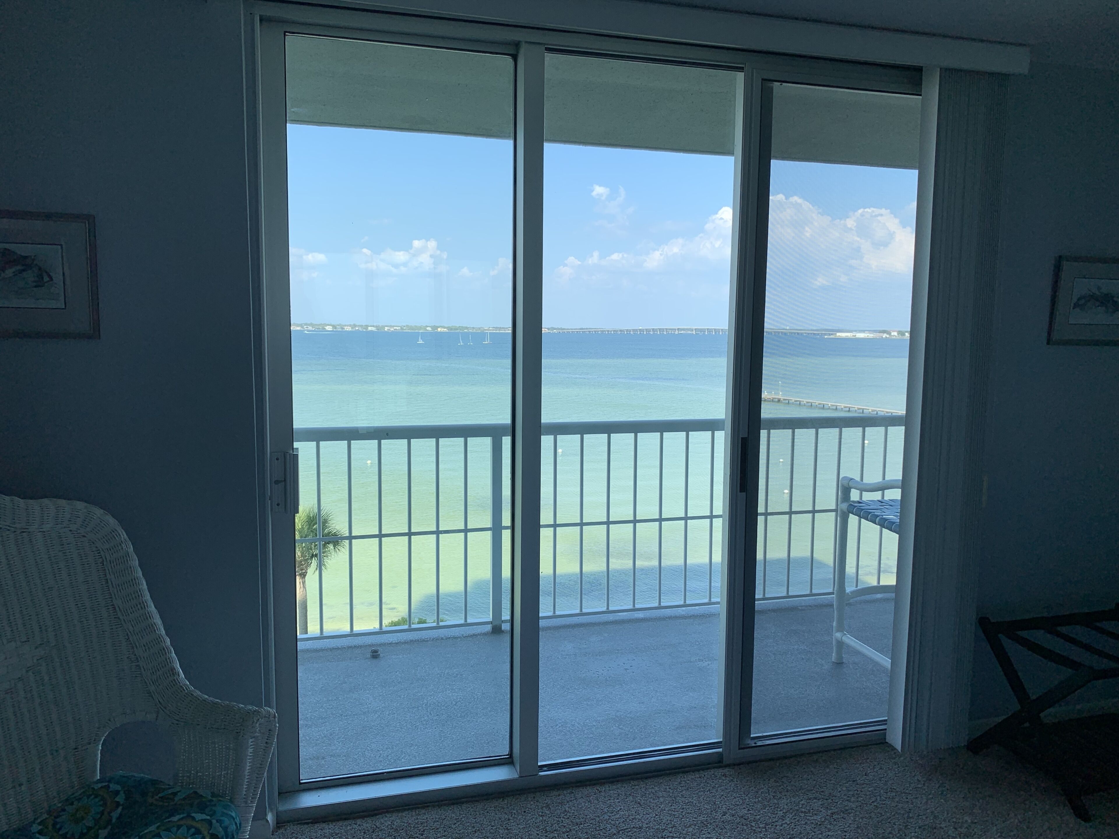 A room with a large sliding glass door leading to a balcony with a view of the sea and a bridge.