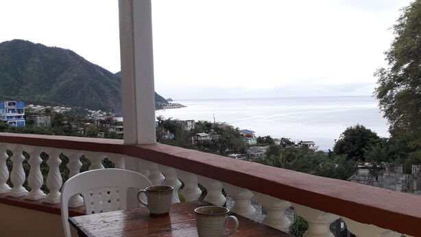 Un balcón con mesa y sillas, con vistas a la costa y montañas a lo lejos.