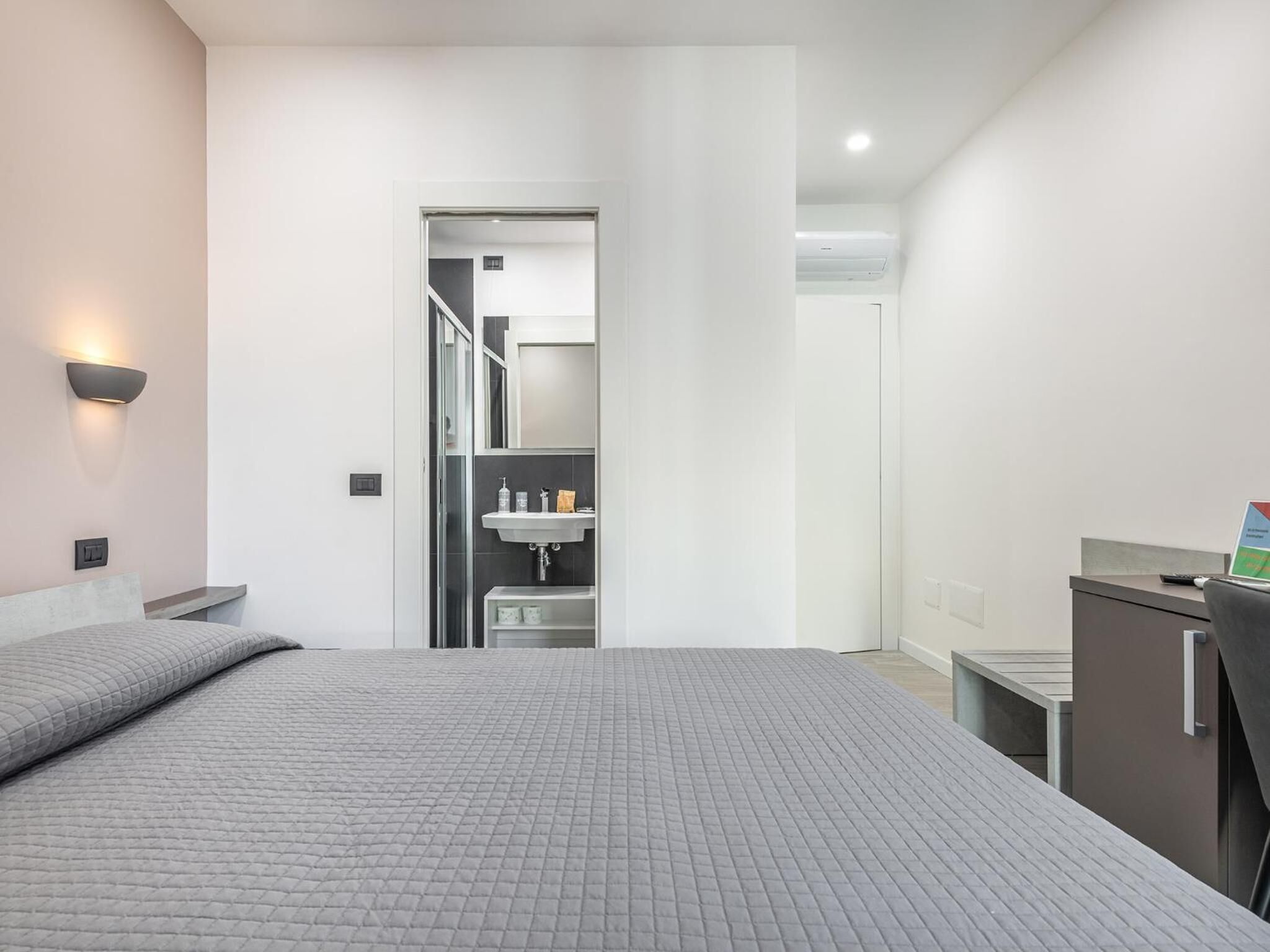 A modern hotel room with a large bed, a desk, and a bathroom visible through an open door.