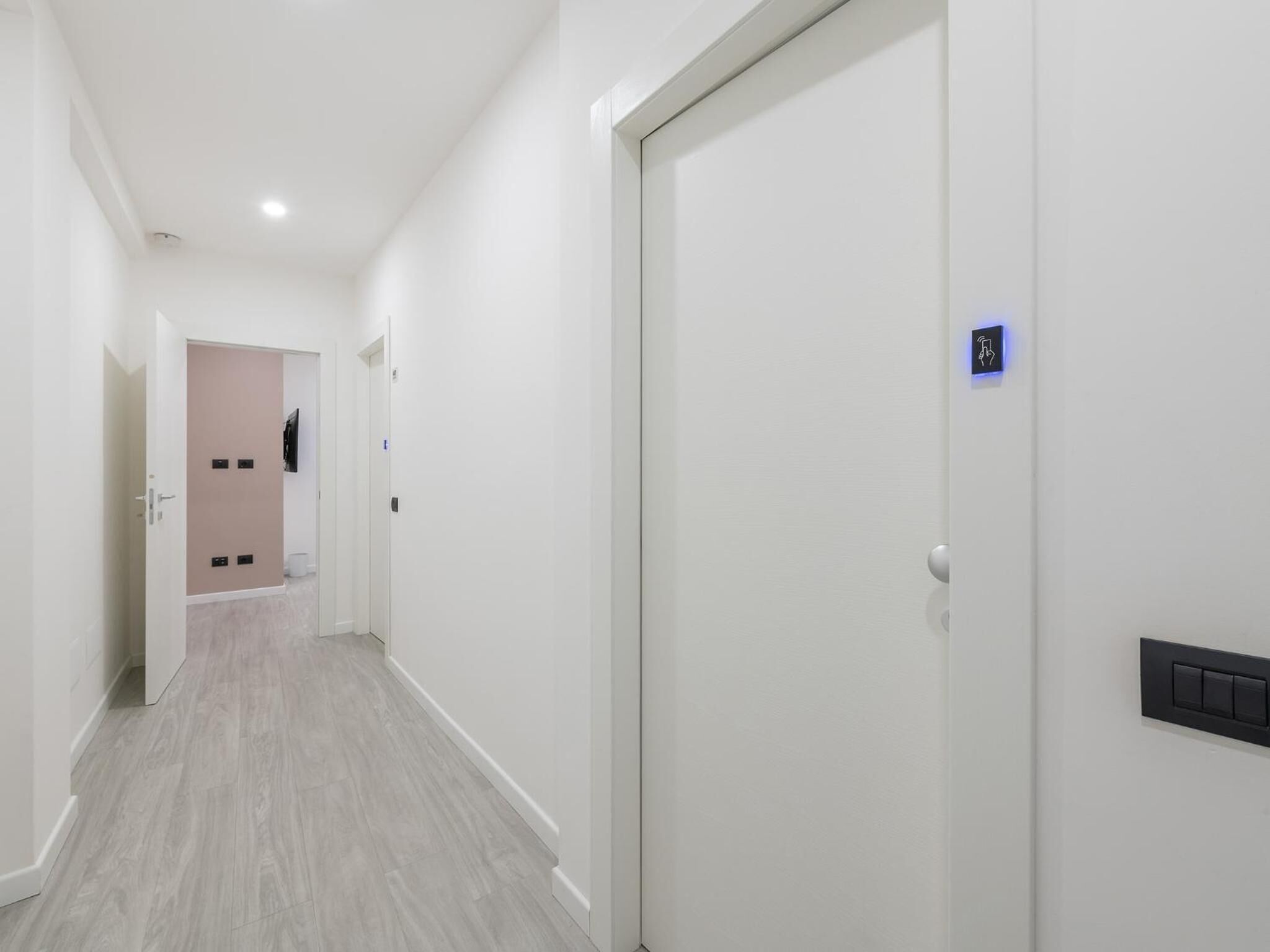 Un pasillo con paredes blancas y suelo de madera que conduce a una habitación con puerta rosa.