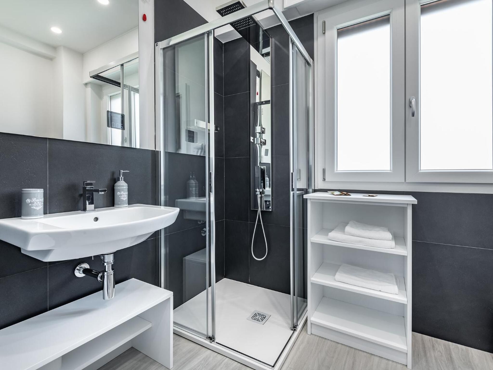 Un baño moderno con ducha envuelta en vidrio, un lavamanos blanco y un estante con toallas.