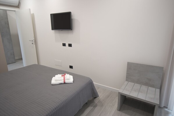 A hotel room with a bed, a TV mounted on the wall, a bench, and a door.