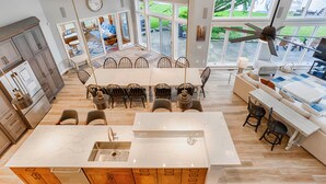 Une cuisine spacieuse dotée d’un grand îlot central, de meubles en bois et offrant une vue sur le jardin arrière grâce à de grandes fenêtres.