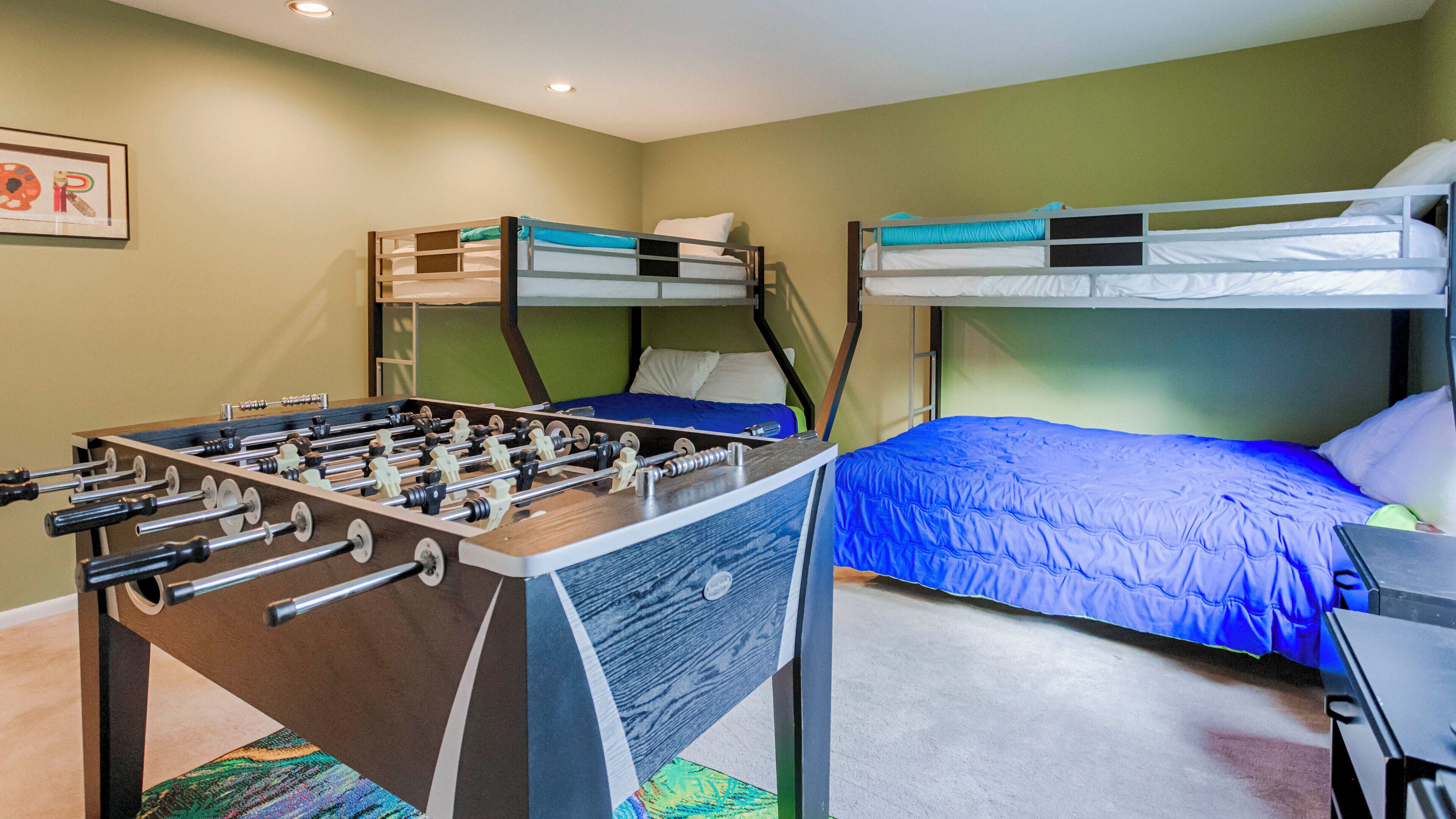 Ein Zimmer mit zwei Etagenbetten, einem Kicker und einem gerahmten Bild an der Wand.