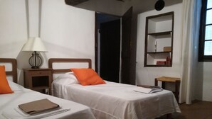 Two single beds with white linens and orange pillows, a bedside table with a lamp, and a small wooden nightstand. - rental house in the Luberon (ROUSSILLON)
