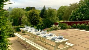 Une table de pique-nique installée à l’extérieur, avec plusieurs bancs et tables, entourée de verdure et d’arbres.