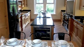 Une cuisine moderne avec des meubles en bois, un îlot central doté d’un évier et un coin repas aménagé pour six personnes, avec des verres à vin.