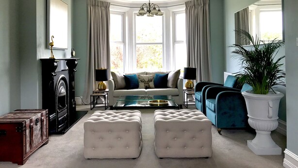 Un salon avec une cheminée, un canapé, des poufs, une table basse et une plante en pot.