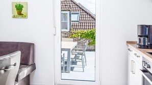 A modern kitchen with a coffee maker, a dining area with a table and chairs, and a view of a house through a glass door. - Seeteufel by Interhome (Norddeich)