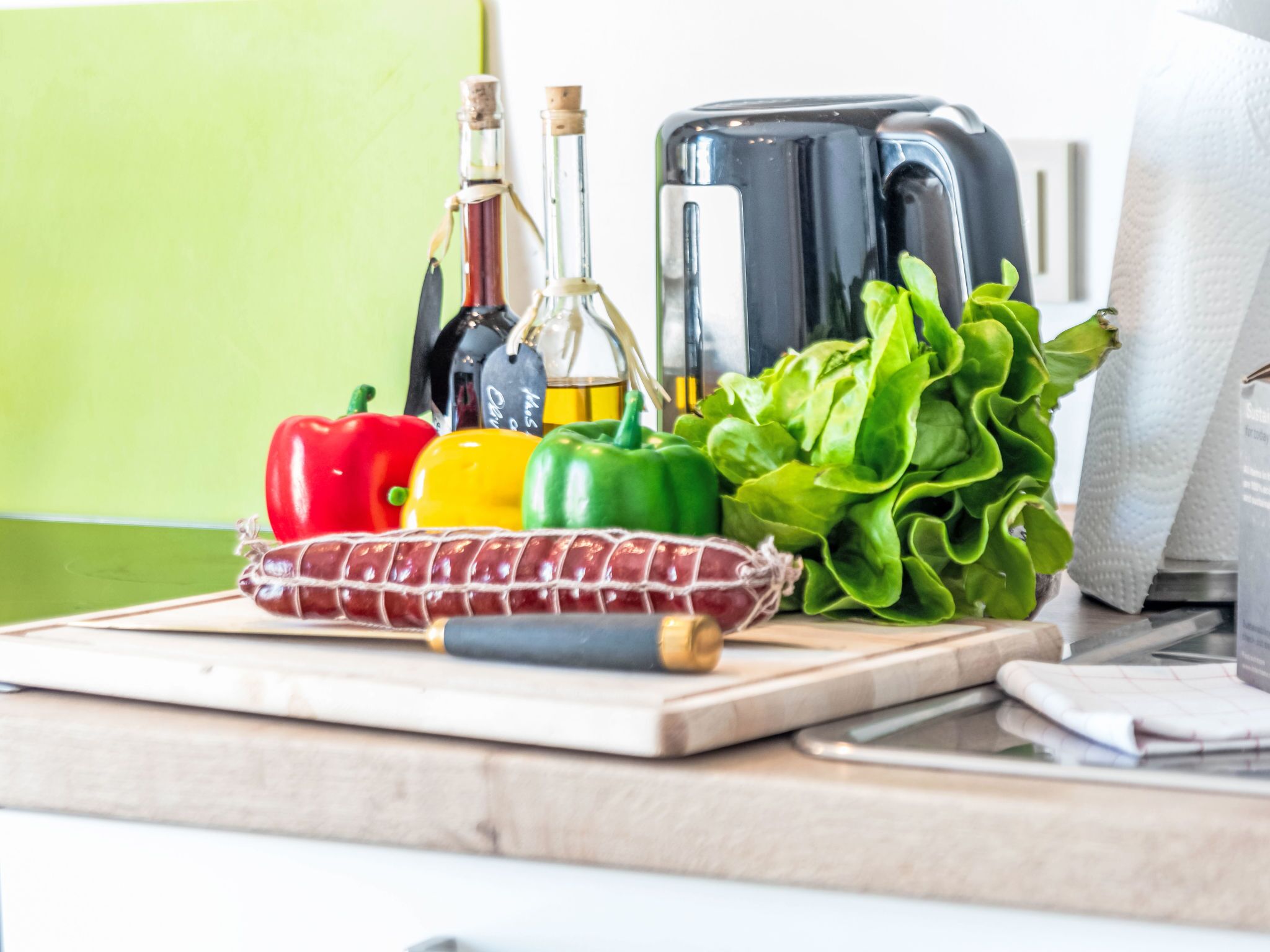 A kitchen counter with a variety of fresh vegetables, a loaf of bread, and a toaster.