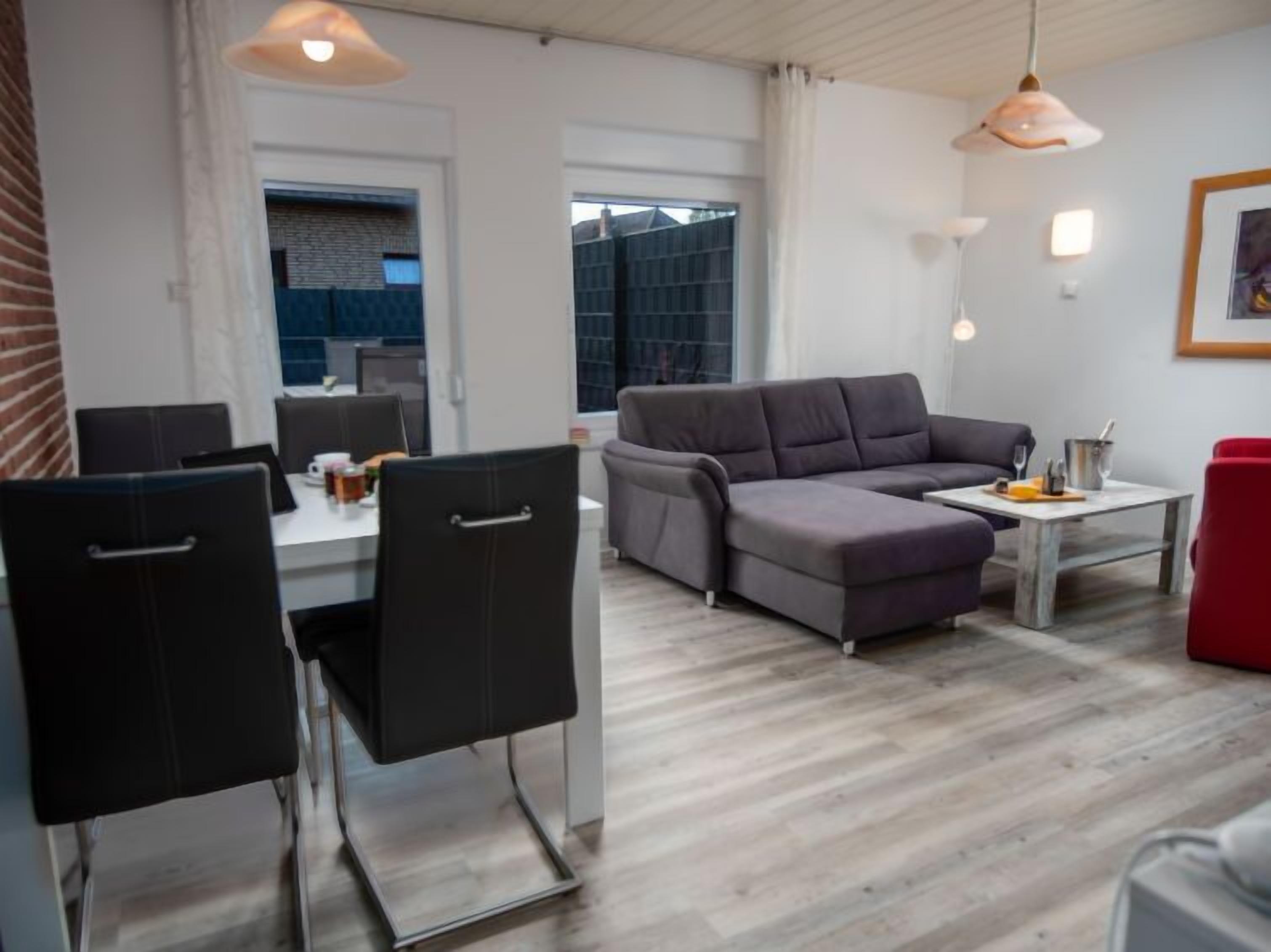 A modern living room with a grey sectional sofa, a dining table with chairs, and a red chair.