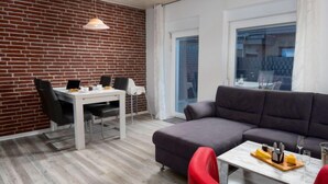 A modern living room with a brick wall, a grey sofa, a dining table with chairs, and a red armchair. - Steuerbord by Interhome (Norddeich)