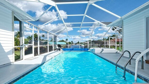 Una piscina interior con agua azul cristalina, rodeada por una estructura blanca con paneles de vidrio y barandillas de metal.