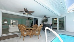 Un patio exterior con piscina, muebles de mimbre, ventiladores de techo y puertas correderas de cristal que dan a una sala de estar.