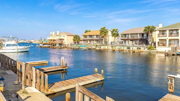 A marina with wooden docks, a white yacht, and beachfront buildings with balconies.