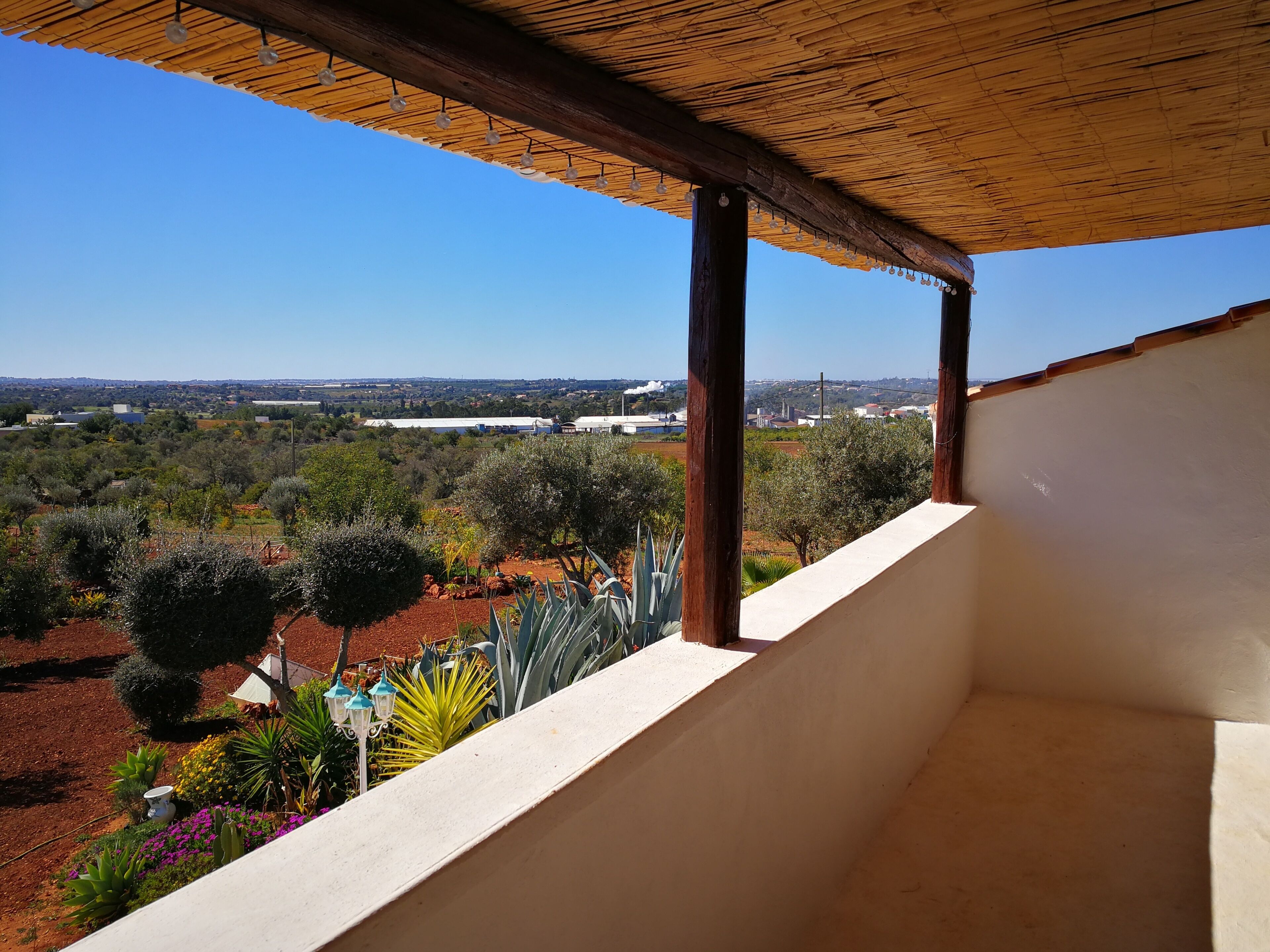 Un balcon donnant sur un jardin aménagé et sur des bâtiments situés au loin.