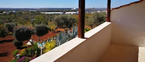 Un balcon donnant sur un jardin aménagé et sur des bâtiments situés au loin.